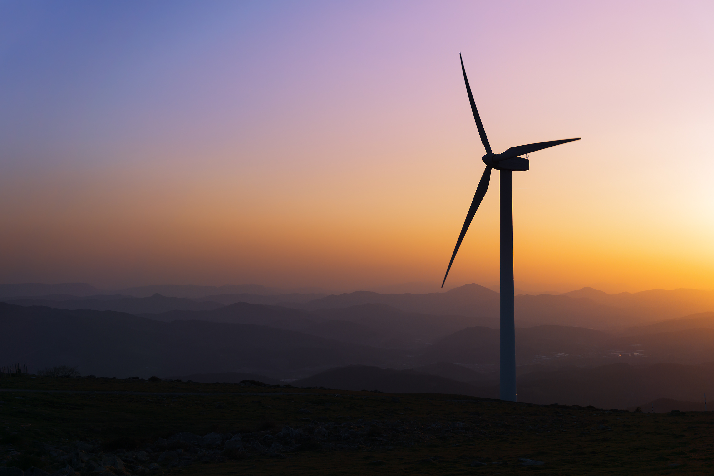 Wind turbine silhouetted against a sunset over the mountains
